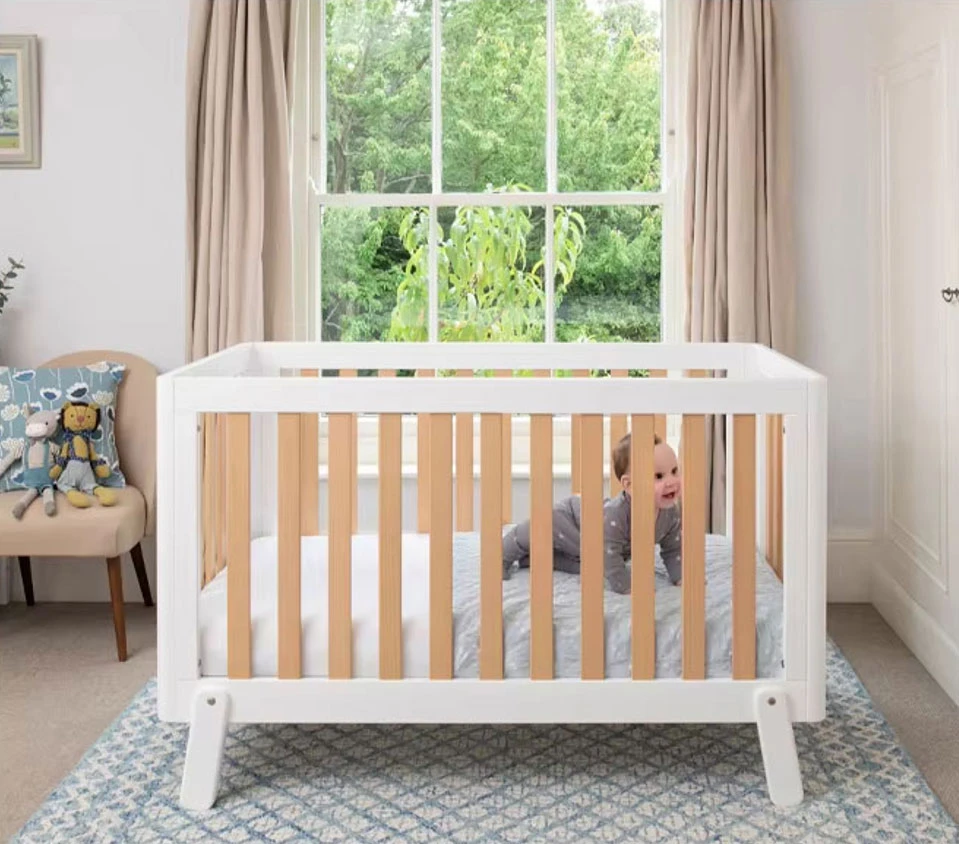 Baby crawling on the mattress inside a white wooden cot bed with natural slats, round corners and angled feet Baby crawling on the mattress inside a white wooden cot bed with natural slats, round corners and angled feet